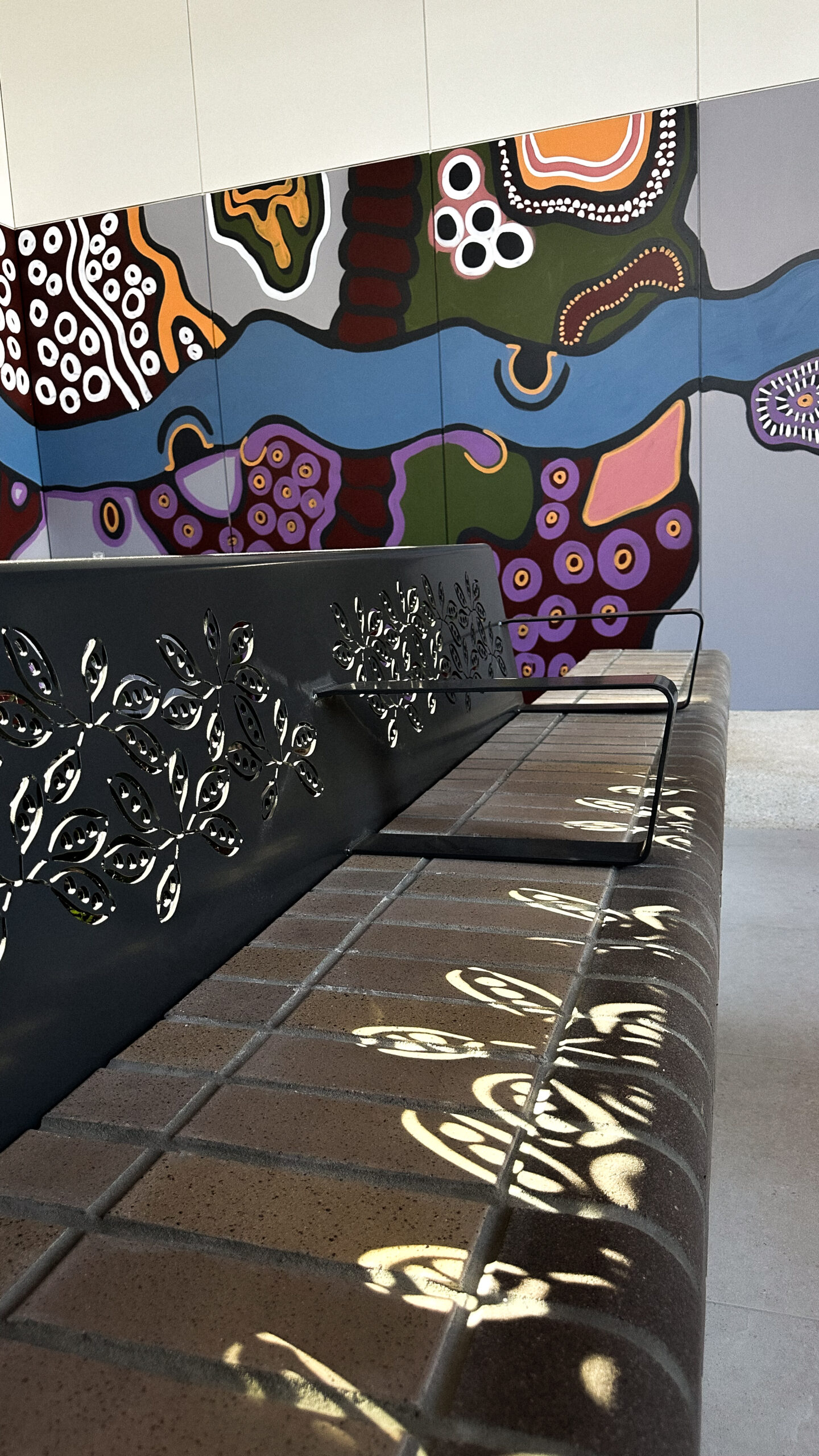Brick seat with decal from metal shining on the seat's surface and a Connecting to Country mural in the background.
